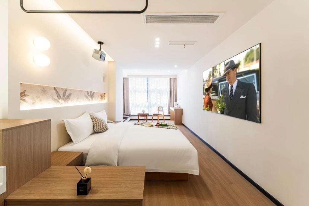 Una habitación de hotel con una cama, una mesita de noche y un ventanal amplio.