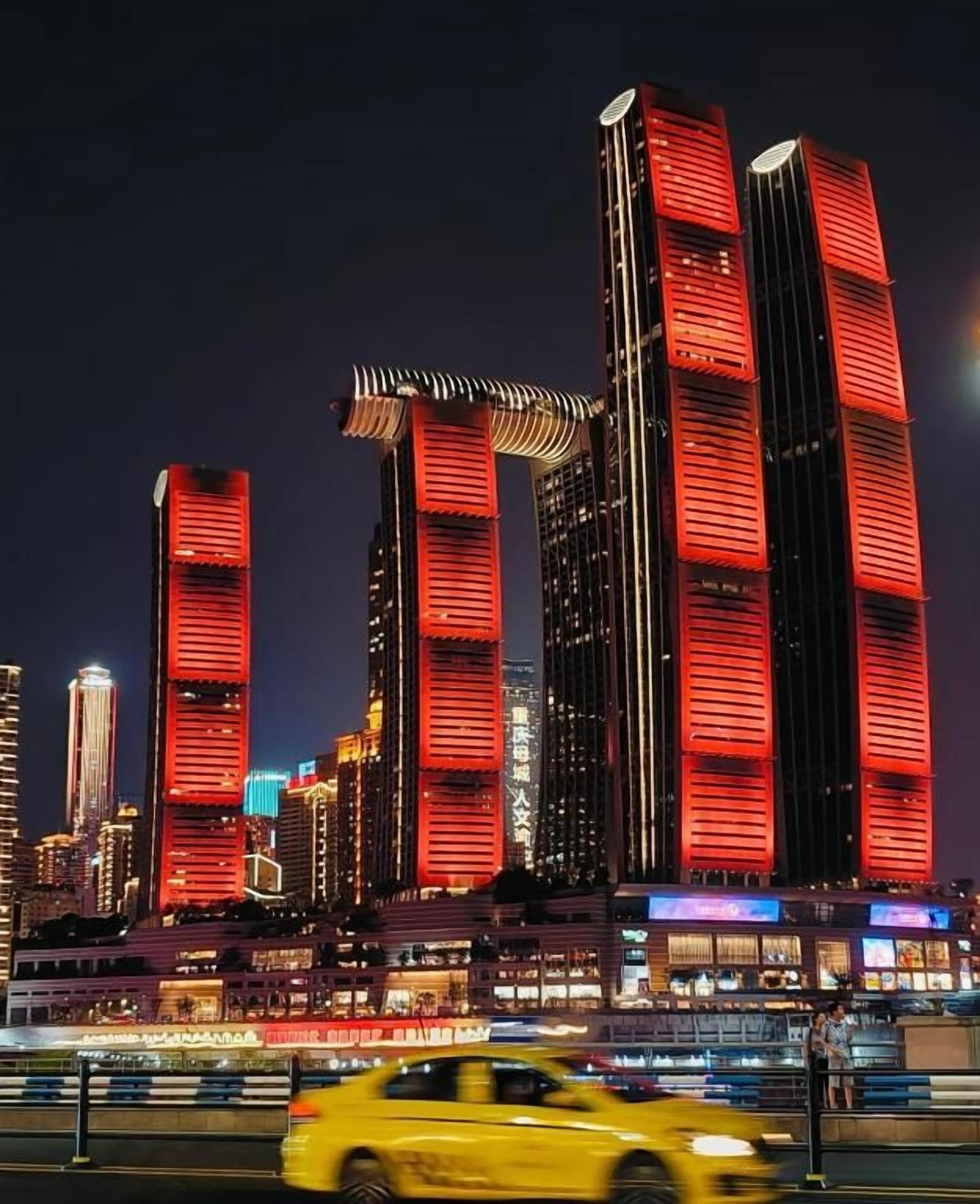 A cityscape at night with illuminated skyscrapers, a moving yellow taxi, and a busy street.