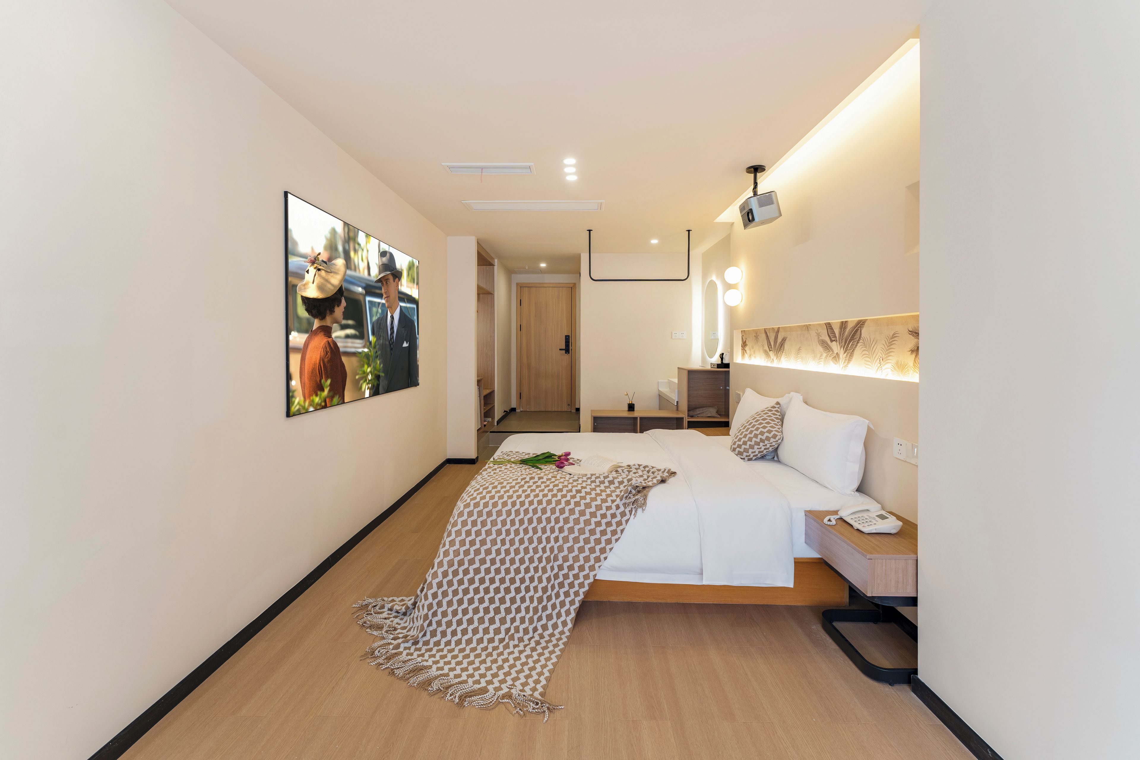 A hotel room with a bed, bedside table, phone, and a mirror.