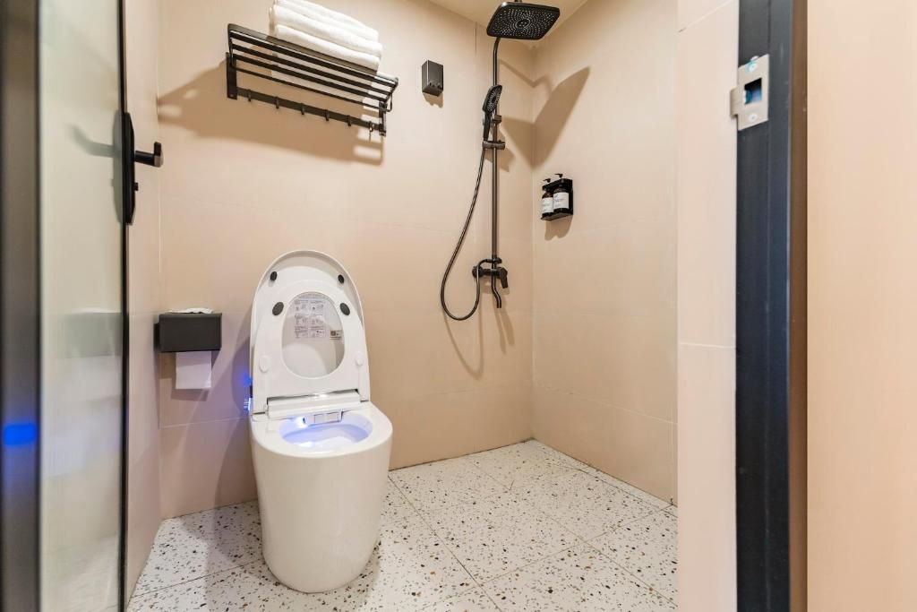 A small, private bathroom with a toilet, a shower, and a towel rack.
