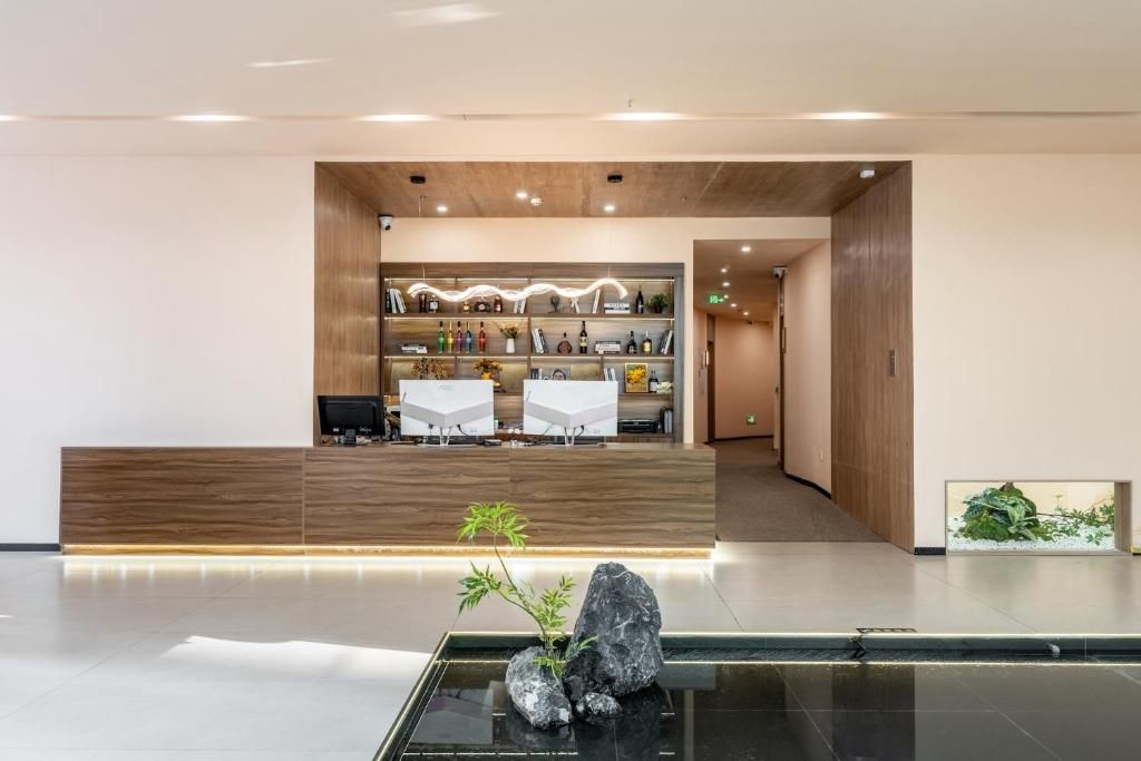 Una zona de recepción con mostrador de madera, un área de estar con mesas blancas y una exhibición de diversos objetos en estanterías.