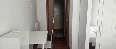 A room with a white desk, a chair, a wardrobe, and a door leading to another room.