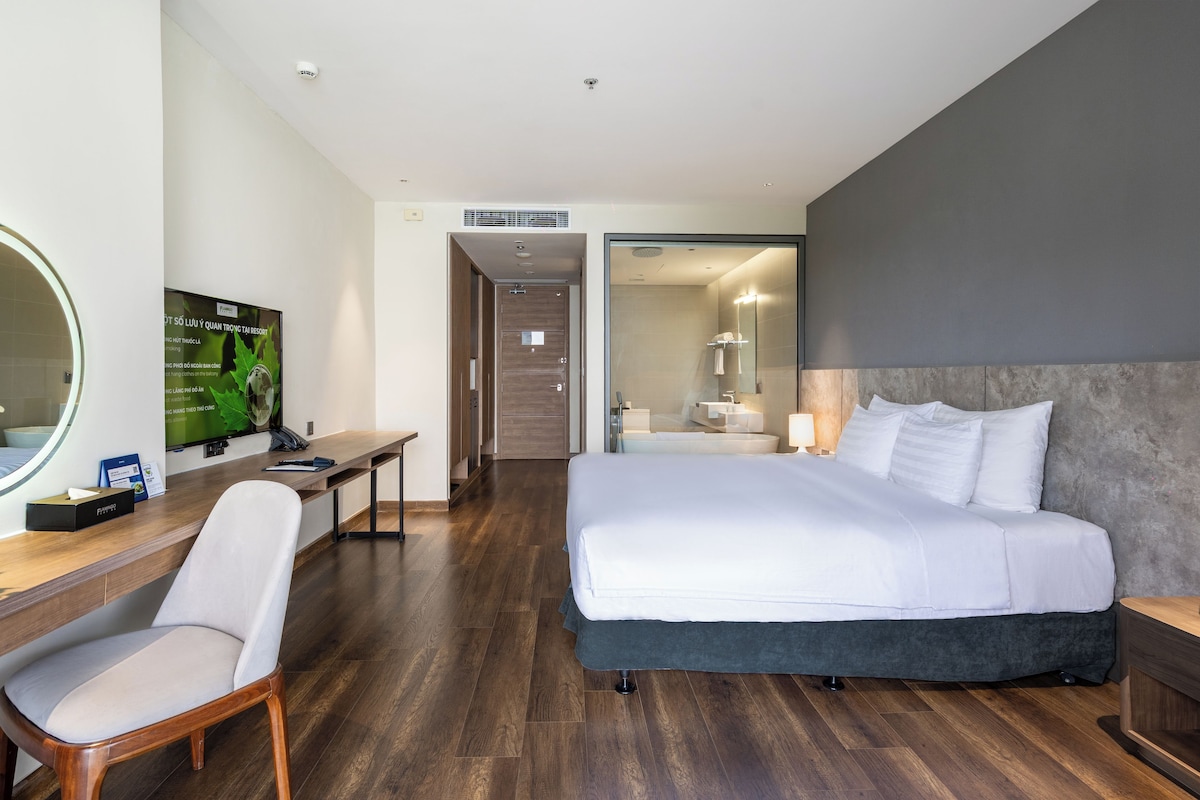A hotel room with a bed, a desk, a chair, a television, and a bathroom visible through an open door.