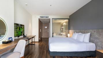 A hotel room with a bed, a desk, a chair, a television, and a bathroom visible through an open door.
