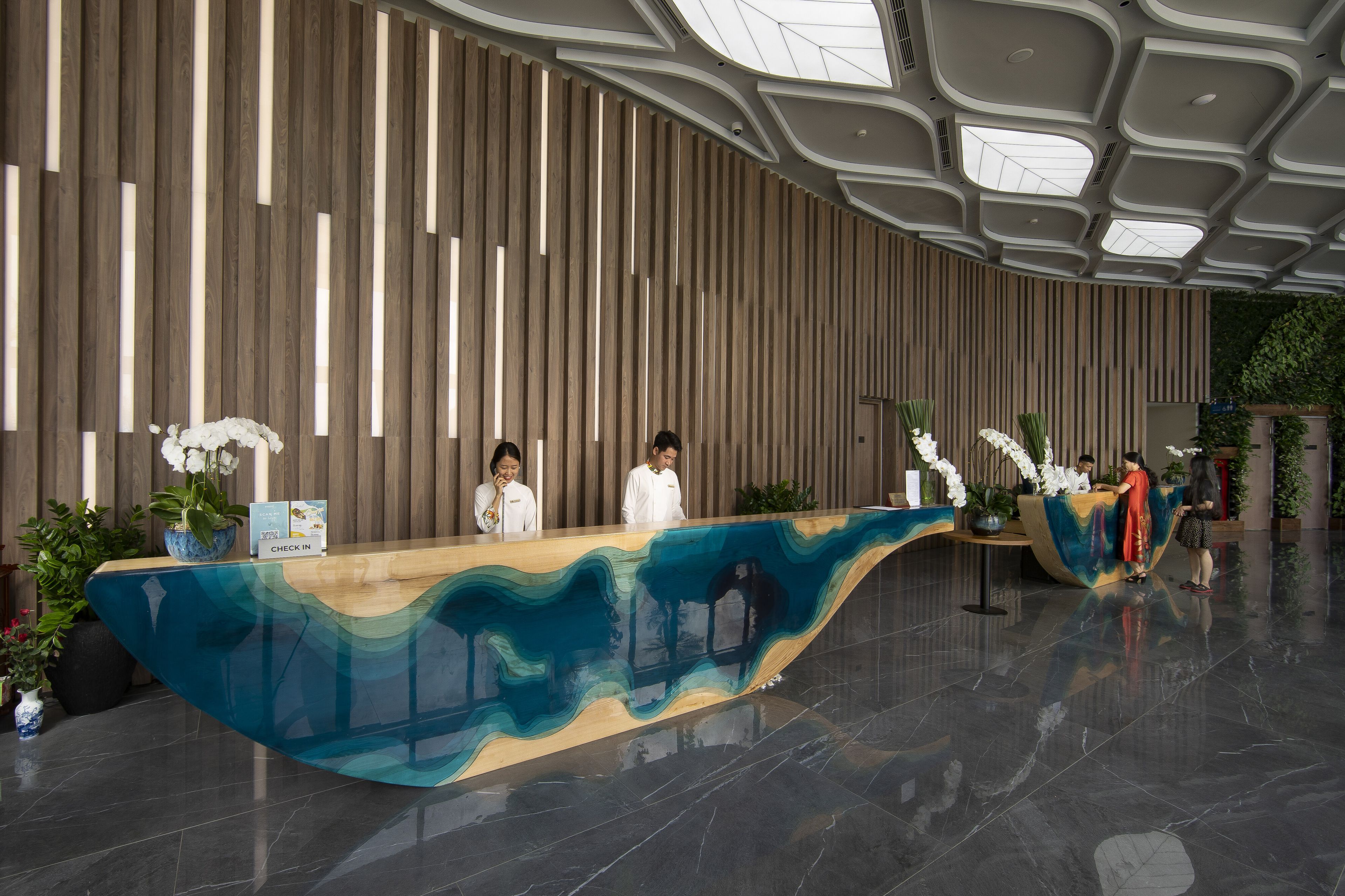 A modern reception desk with a wavy design, a high ceiling with skylights, and a vertical wooden panel wall.