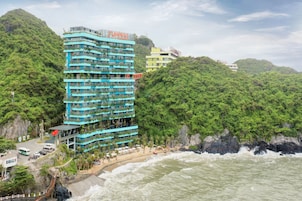 A multi-story hotel with balconies, a beach, and a rocky coastline.