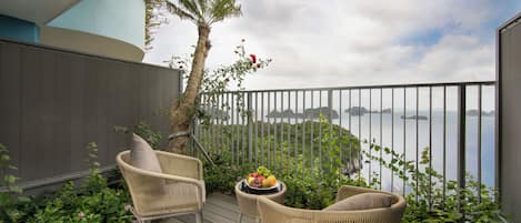 Ein Balkon mit Korbstühlen, einem kleinen Tisch mit Obst und Blick auf Meer und Berge.