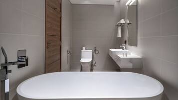 Un baño moderno con una bañera independiente, inodoro y lavamanos con espejo.