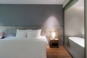 A modern hotel room with a large bed, bedside lamp, and a separate bathroom with a bathtub. - Vela Cat Ba Beach Resort - Flamingo Sea & Sand (Cat Hai)