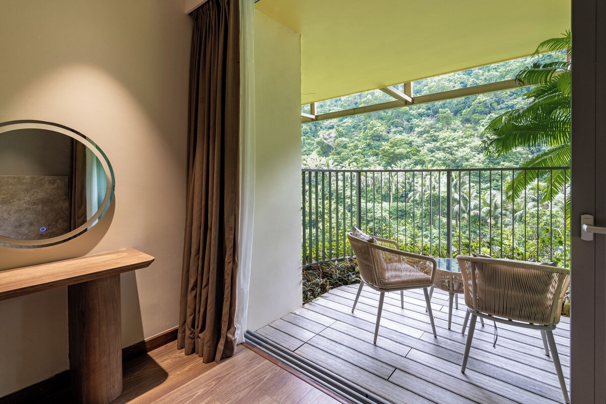 A balcony with a view of a lush green landscape, a round mirror, and two wicker chairs.