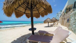 Ein Strand mit weißen Liegestühlen, einem Reetdachschirm und freiem Blick auf den Ozean.