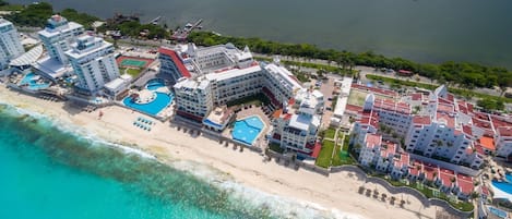 Un hotel frente al mar con varias construcciones, una playa y una zona de piscina.
