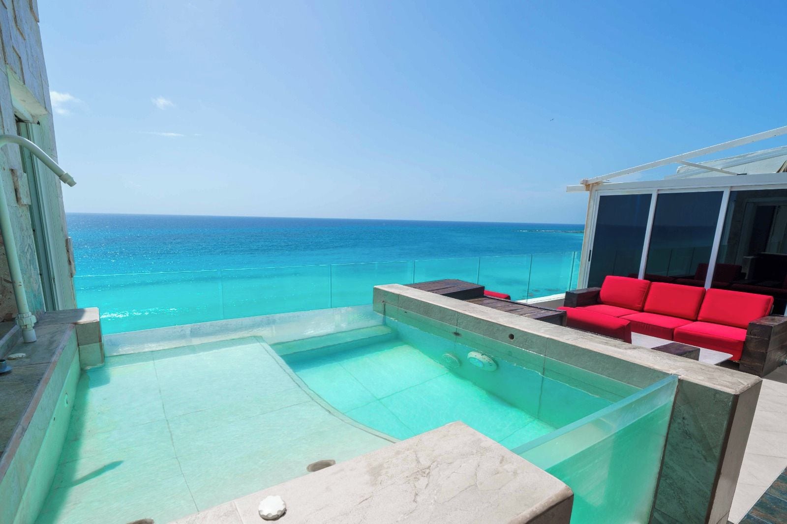 Un espace piscine sur le toit, doté d’une balustrade en verre, d’un canapé rouge et offrant une vue dégagée sur l’océan.