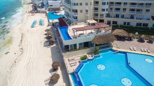 Ein Resort mit einem großen Swimmingpool, Liegestühlen am Strand und Blick auf den Ozean.