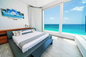 Quarto moderno com uma cama grande, mesa de cabeceira, abajur e vista para o oceano.