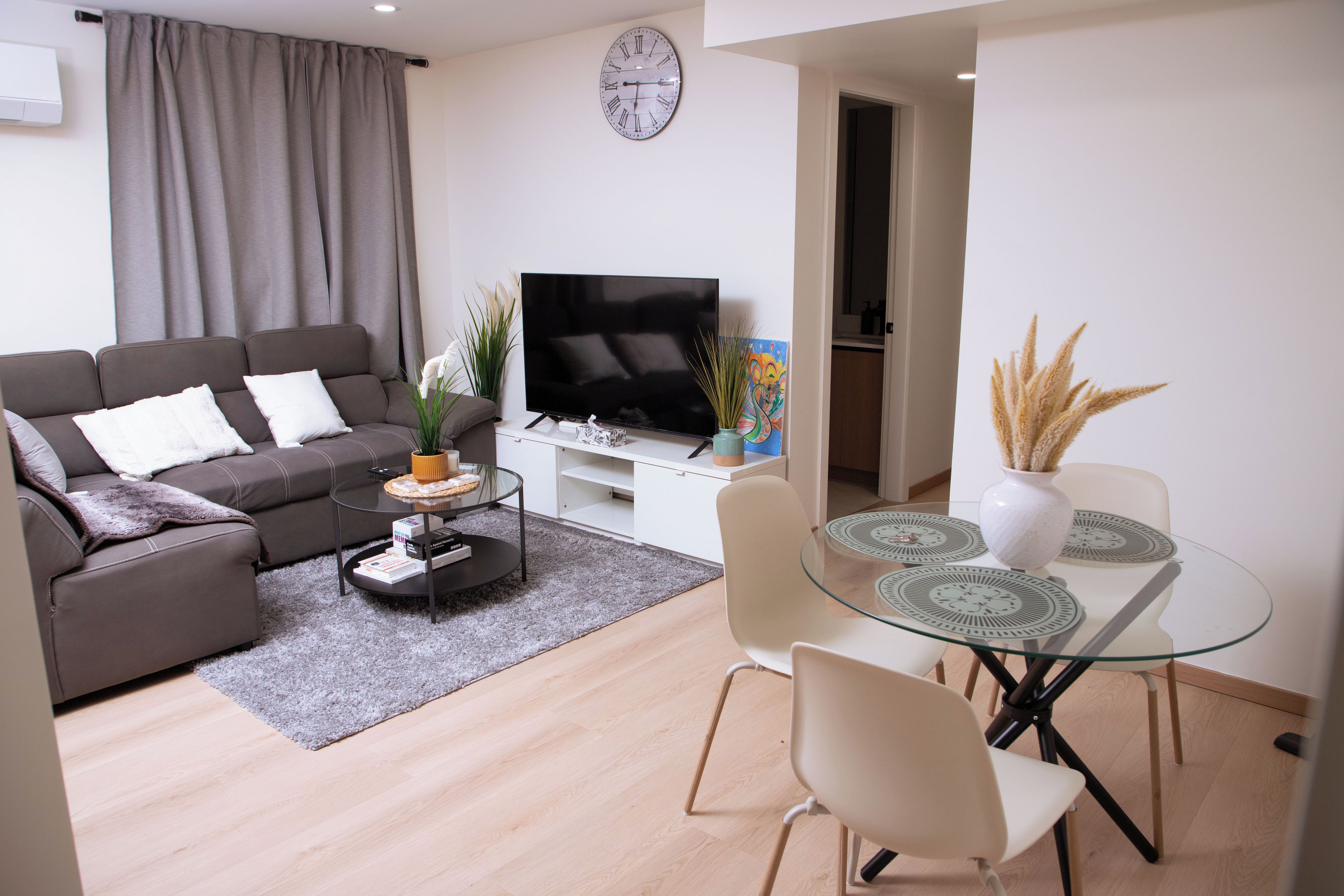 Una sala de estar moderna con sofá, televisión, mesa de centro y zona de comedor con sillas y mesa de vidrio.