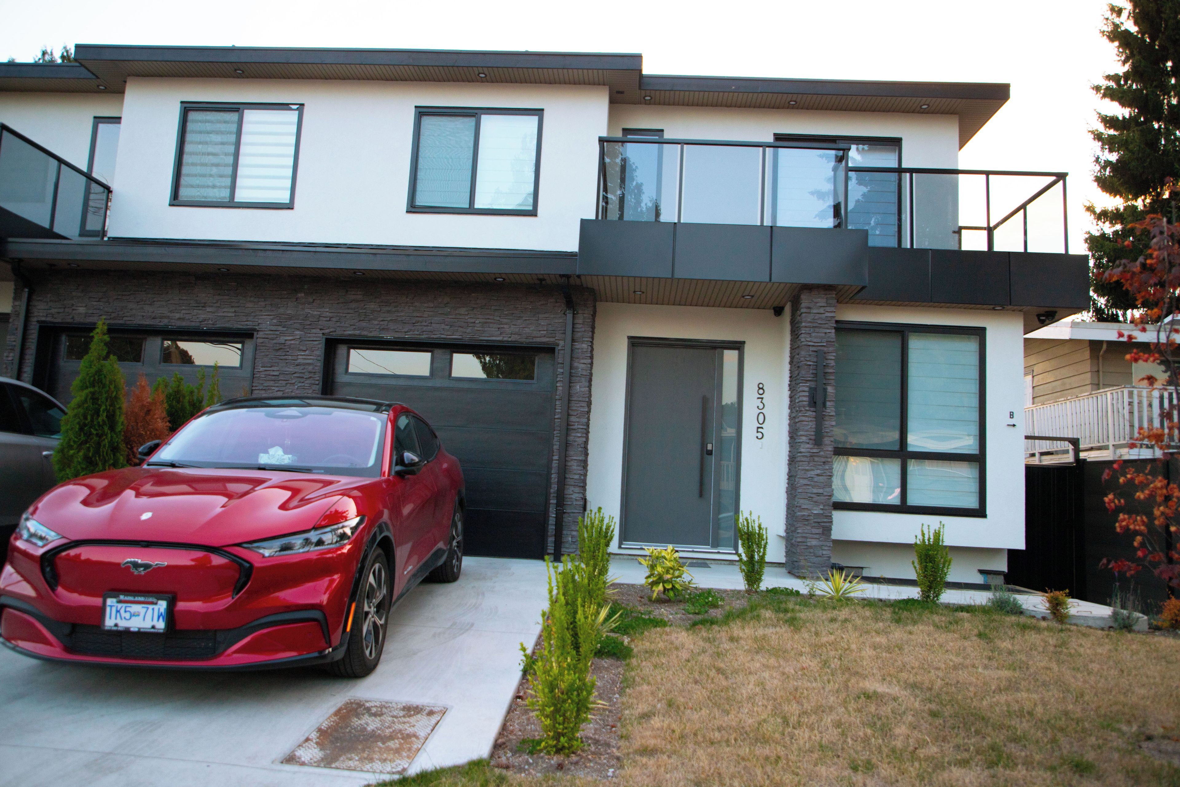 Una casa moderna de dos pisos con un coche rojo estacionado en la entrada.