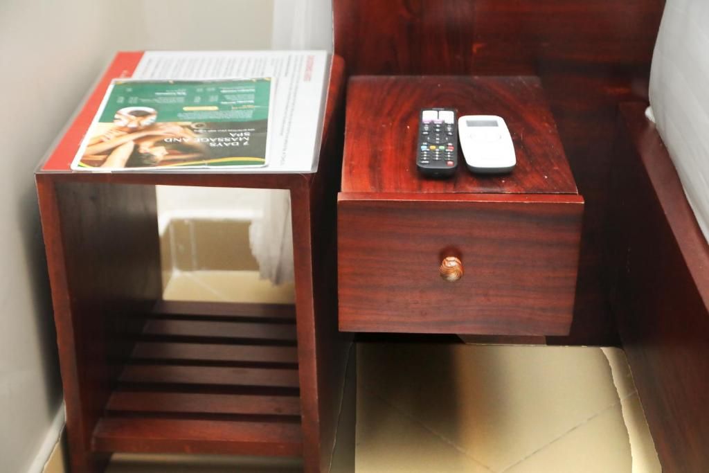 A wooden nightstand with a remote control and a book.