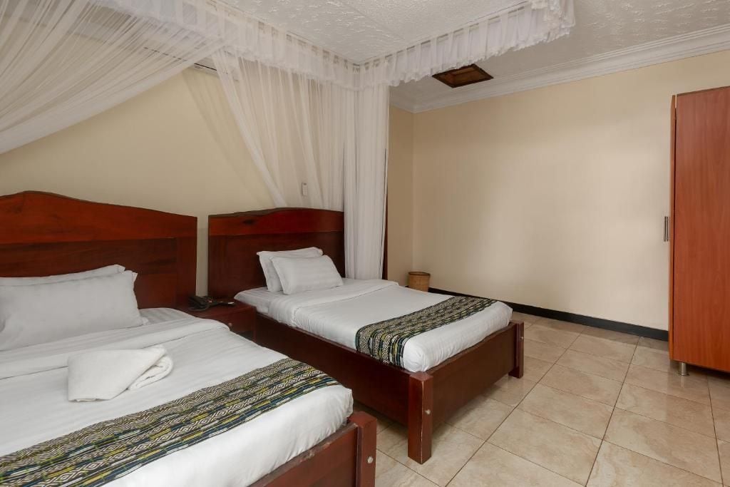 Habitación de hotel con dos camas individuales, un armario de madera y una mosquitera.