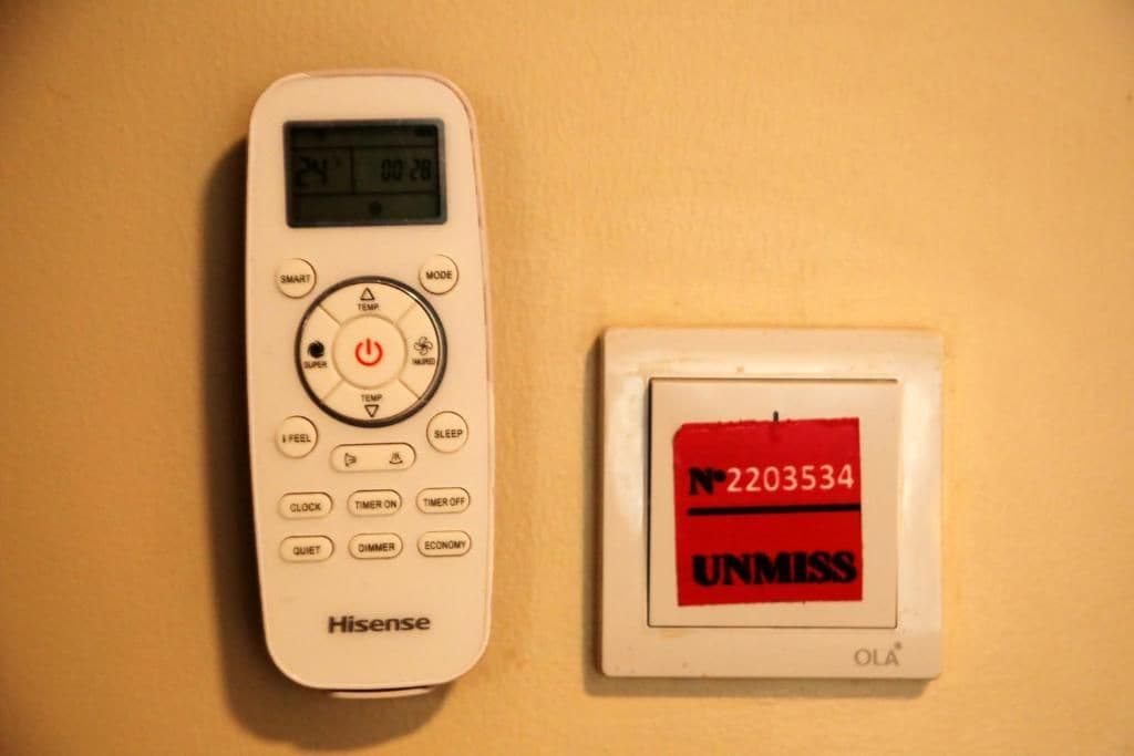 A Hisense remote control and a wall-mounted thermostat with a red sticker.