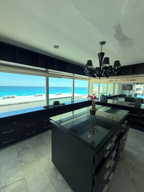 A modern kitchen with a large island, a view of the beach, and a chandelier. - Luxury Oceanfront Suite with Jacuzzi (Cancún)