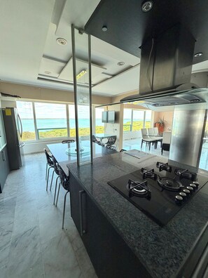 A modern kitchen with a central island, stainless steel appliances, and a view of the sea. - Luxury Oceanfront Suite with Jacuzzi (Cancún)