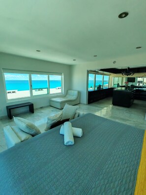 A modern bedroom with a large bed, a seating area with a sofa and armchairs, and a view of the ocean. - Luxury Oceanfront Suite with Jacuzzi (Cancún)