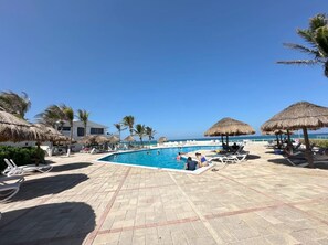 A poolside area with lounge chairs, a swimming pool, and thatched umbrellas. - Luxury beachfront suite with a hot tub (Cancún)