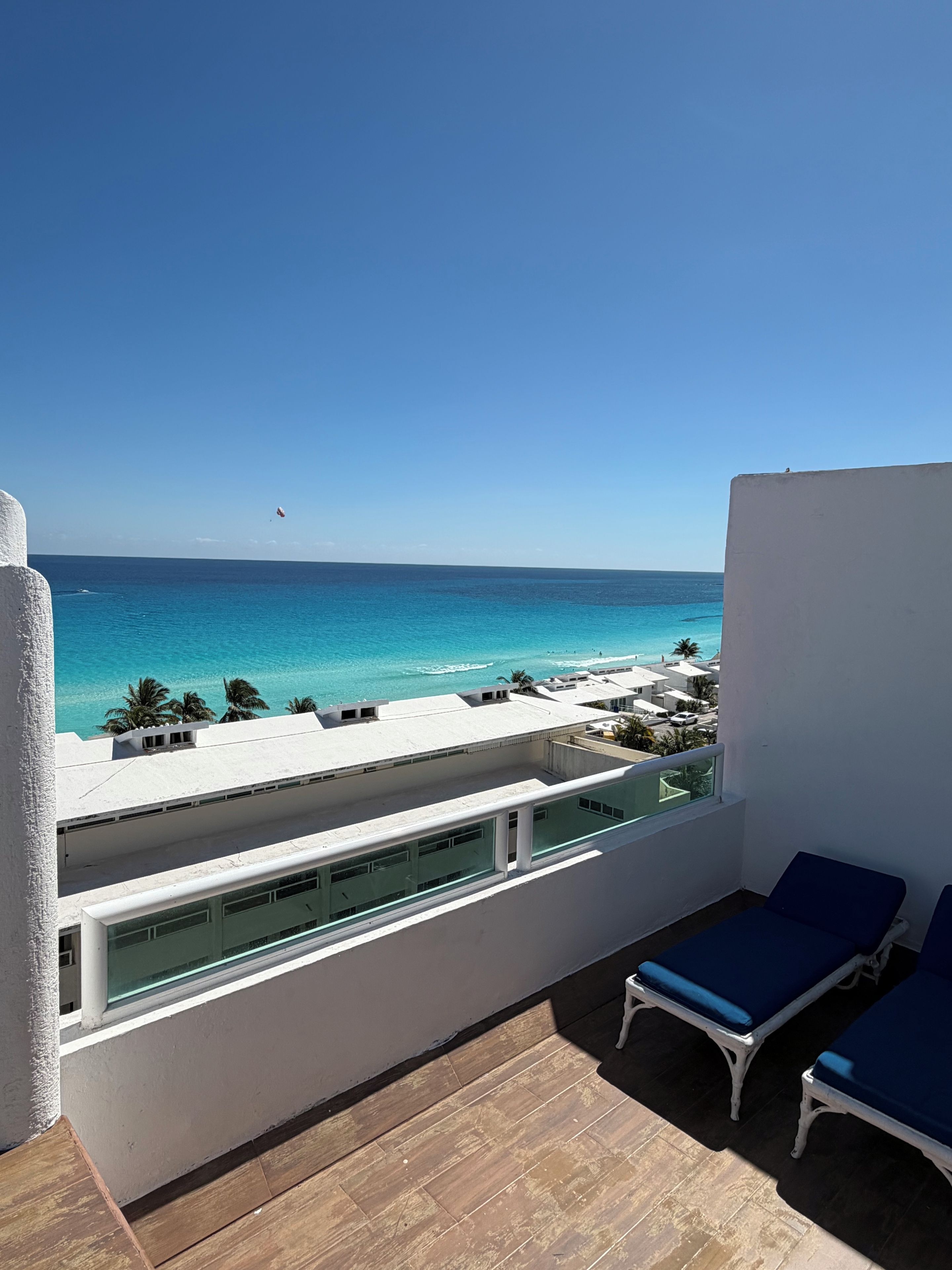 A balcony with a view of the sea, wooden flooring, and two blue lounge chairs.