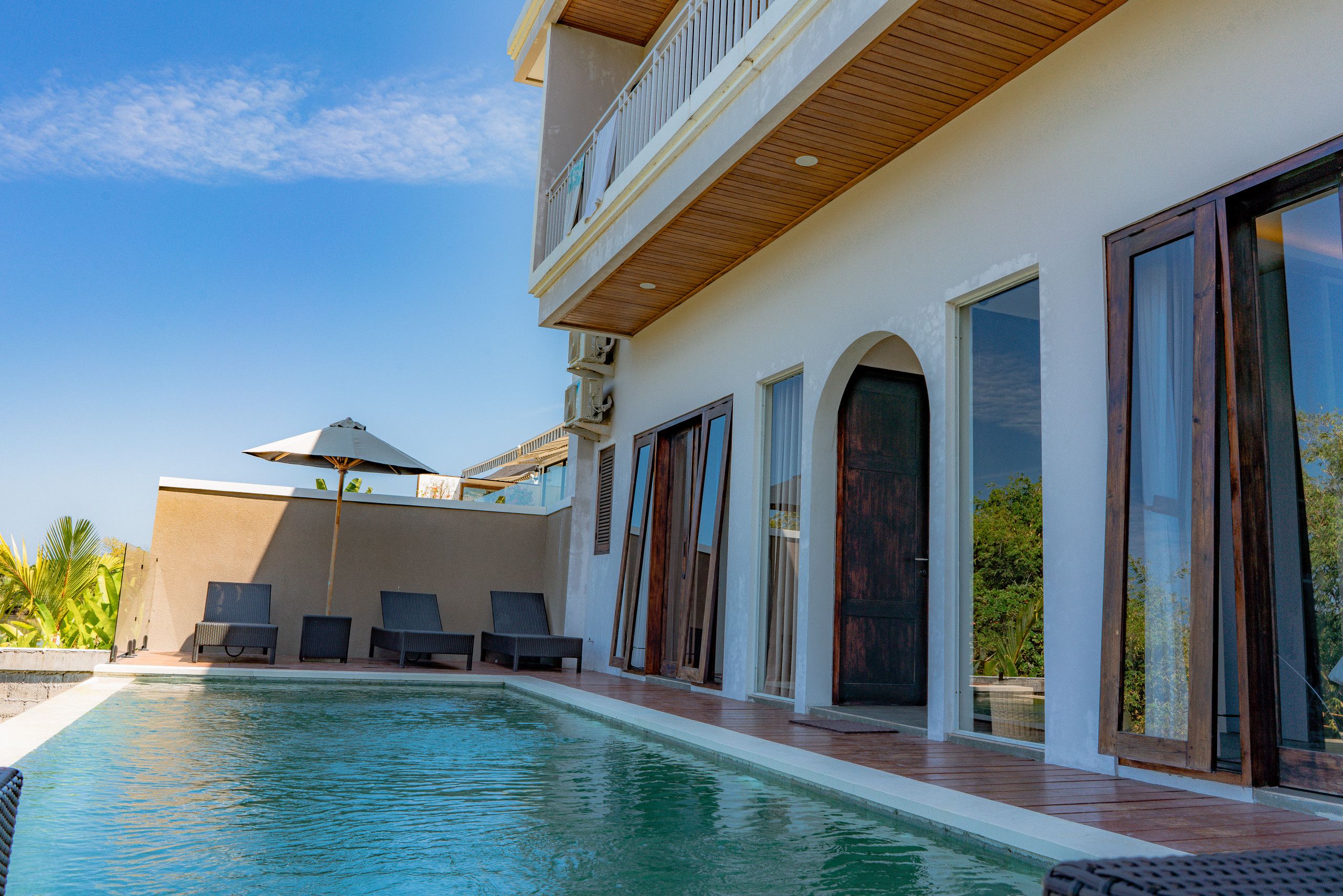 A swimming pool with lounge chairs, a covered seating area, and a building with large windows and doors.