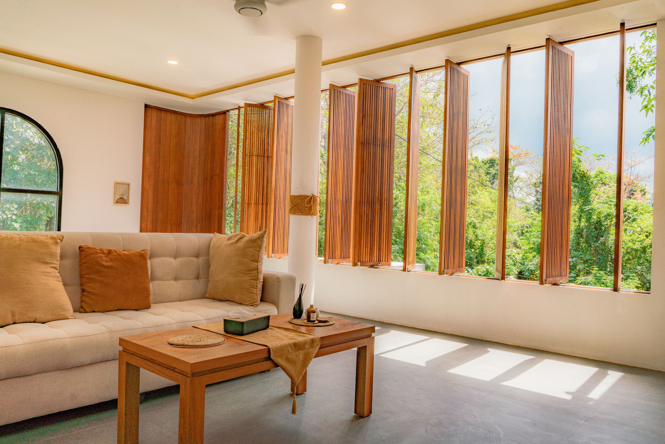 A room with a sofa, a table, and large windows with wooden slats.