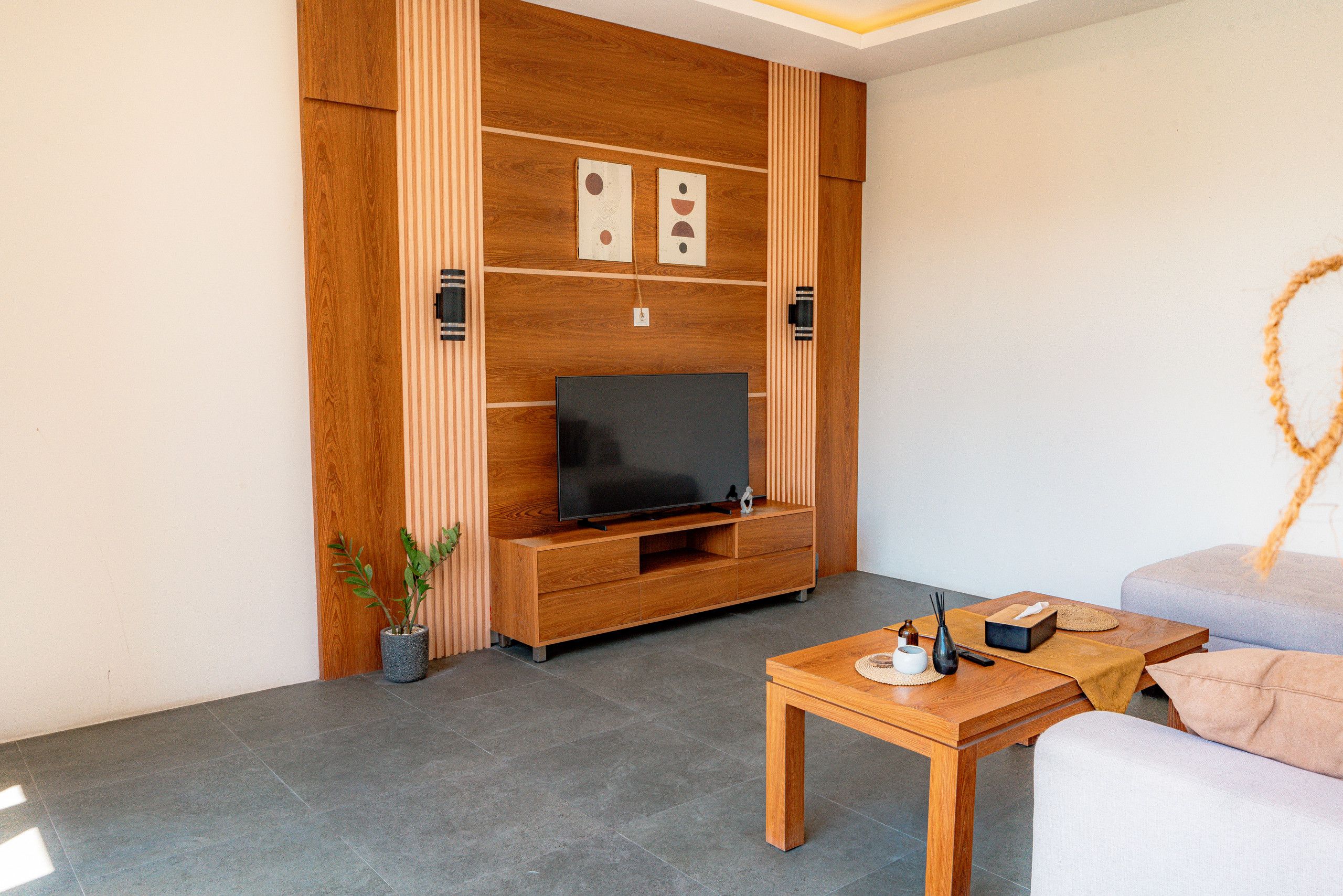Een moderne woonkamer met een houten tv-meubel, een flatscreen televisie, een salontafel en een bank.