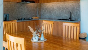 Interior de madeira com mesa de jantar, cadeiras, ventilador de teto e área de cozinha com bancada e pia.