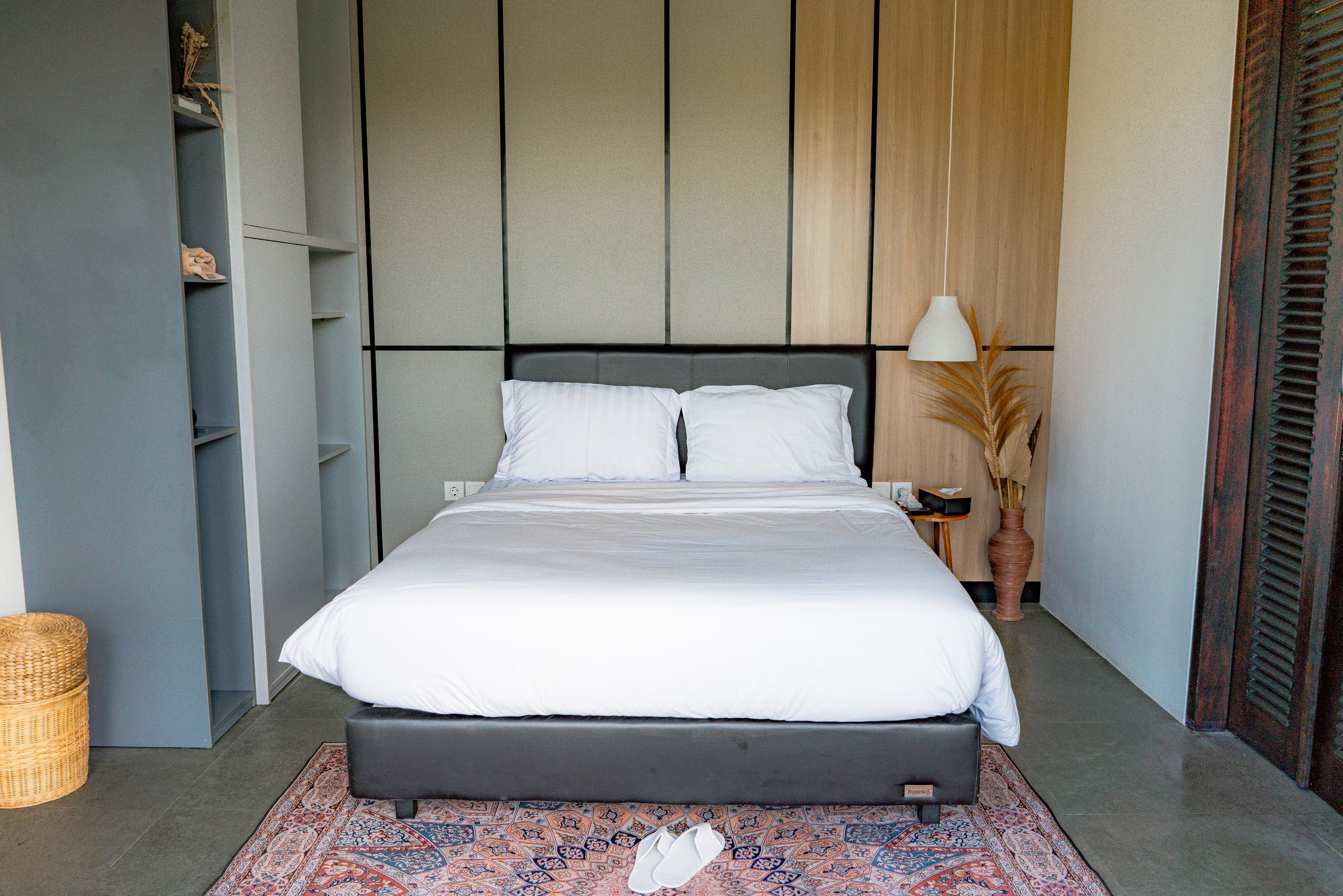 Un dormitorio moderno con una cama grande, una mesita de noche, una lámpara y un jarrón decorativo.