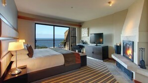 A hotel room with a large bed, a television, a fireplace, and a balcony with a view. - Hyatt Highlands Inn Spa Townhome Sept 19-26, 2026, Carmel Highlands, ocean view (Carmel)