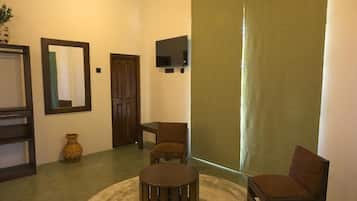 Una habitación con una mesa redonda, dos sillas, un espejo, un televisor y una puerta.