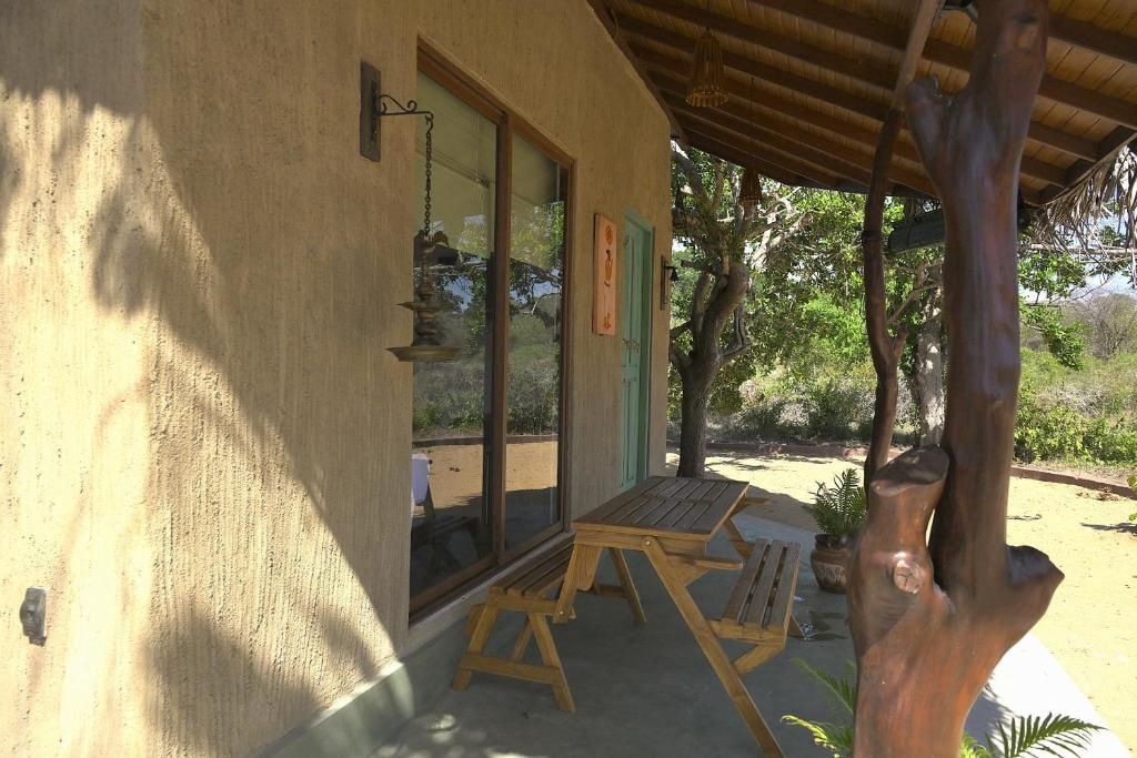 A covered outdoor seating area with a table and chairs, a wooden post, and a door with a green frame.