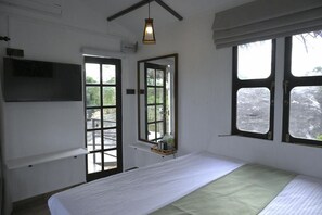 Ein Zimmer mit einem Bett, einem an der Wand montierten Fernseher, einem Fenster mit Blick ins Freie und einer Tür zu einem Außenbereich.