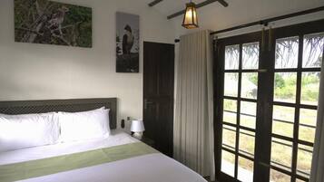Una habitación de hotel con cama, mesita de noche, lámpara, ventana con cortinas y puerta.