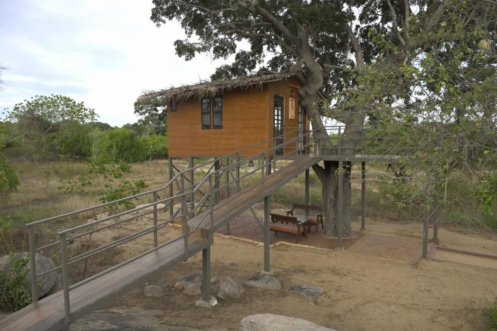 A wooden cabin with a thatched roof, a wooden staircase leading up to it, and a bench outside.