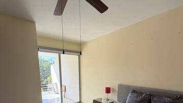 A bedroom with a bed, a ceiling fan, a nightstand with a lamp, and a view of the outside through a sliding door.