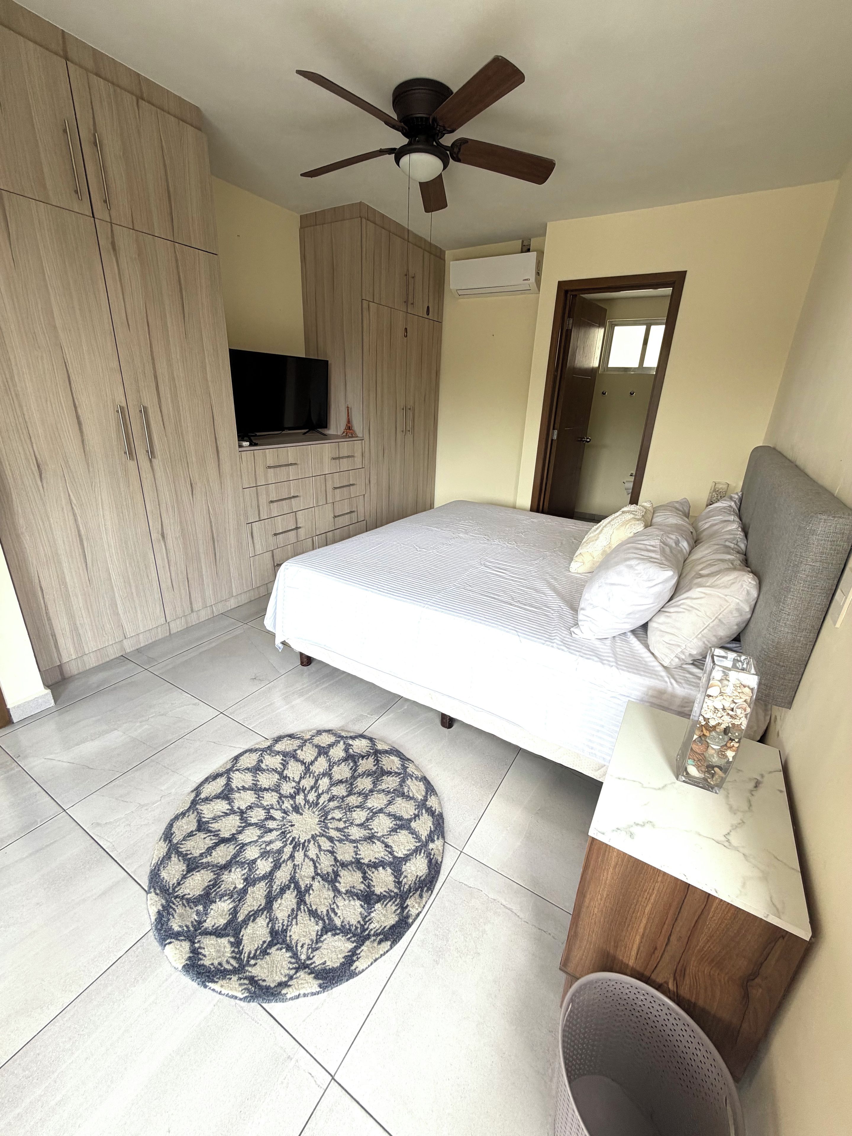 A bedroom with a bed, a ceiling fan, a TV, and a wardrobe.