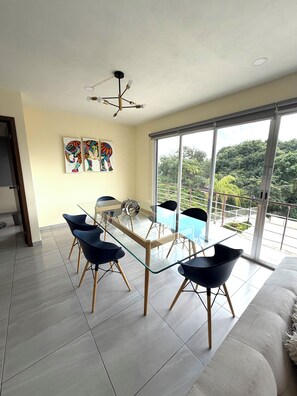 A modern living room with a glass dining table, black chairs, a sofa, and a balcony with a view of greenery. - Luxury apartment with a balcony in the Cumbres shopping plaza (Cancún)