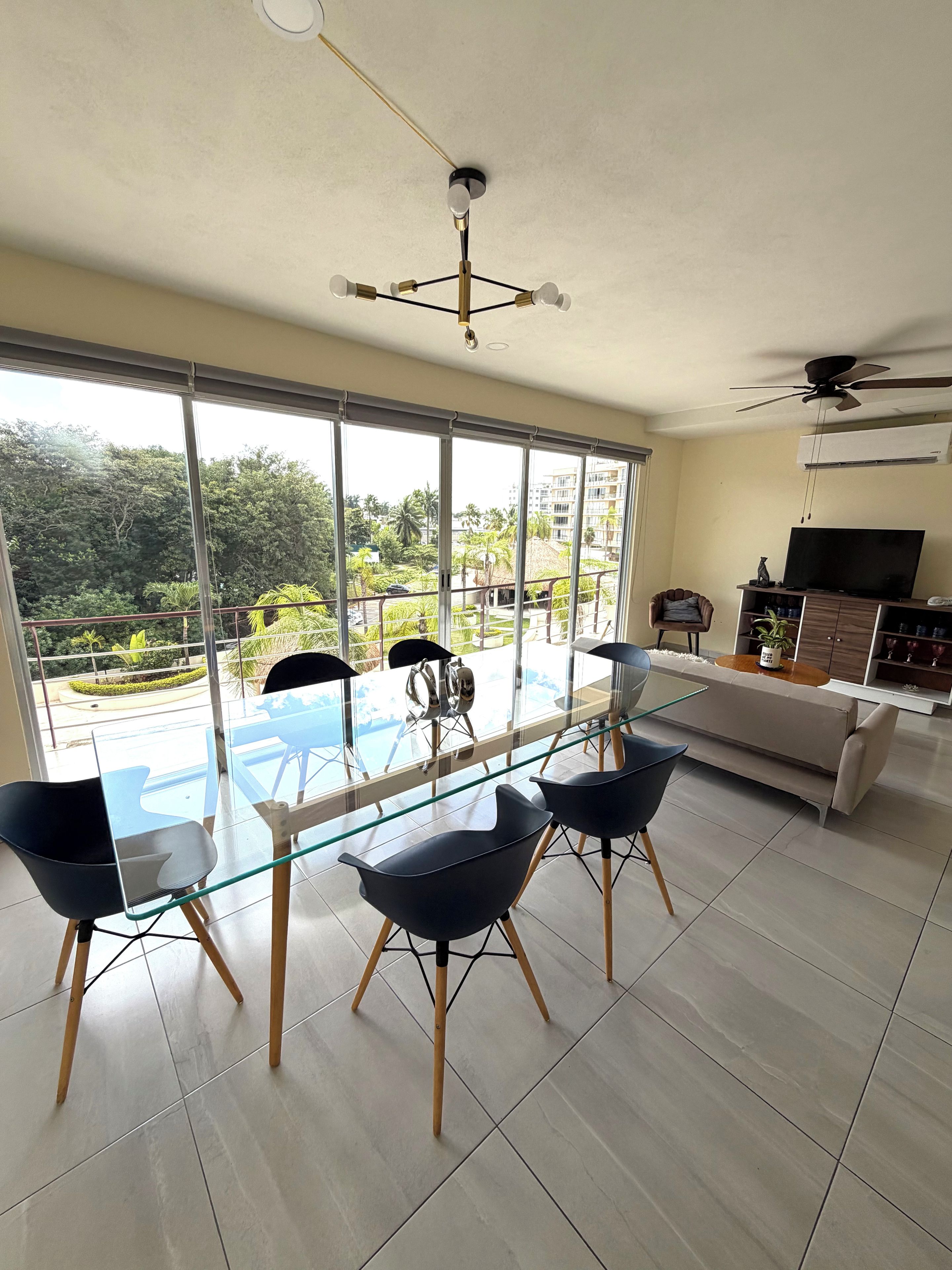 A modern living room with a glass dining table, black chairs, a sofa, and a TV.