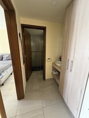 A narrow hallway with a bed, a bathroom with a sink, and a wardrobe. - Luxury apartment with a balcony in the Cumbres shopping plaza (Cancún)