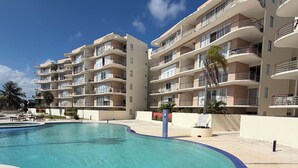 Een meerhoog hotel met een zwembad, balkons en palmbomen.