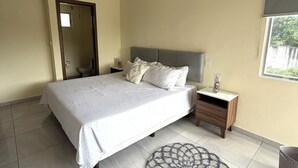 Een slaapkamer met een bed, nachtkastje, ronde vloerkleed, plafondventilator, raam met uitzicht en een airconditioning.