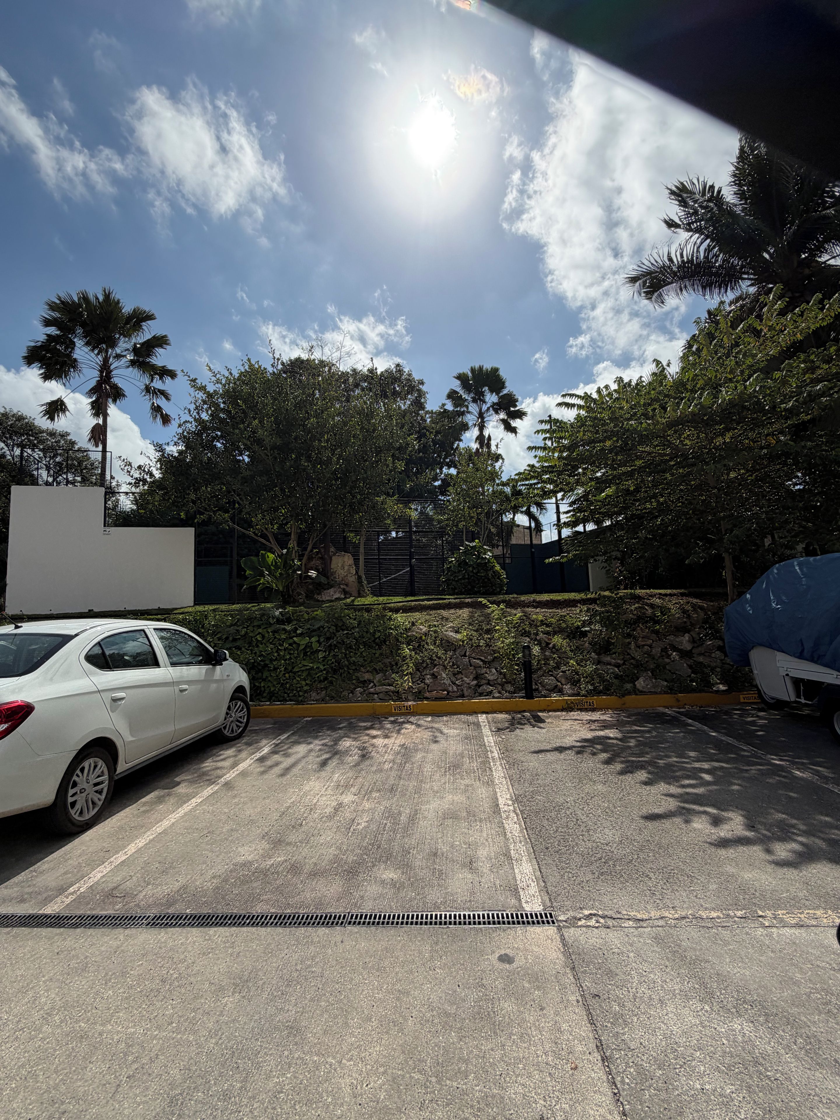 A parking area with a white car, a blue vehicle, and a building with a gated entrance.