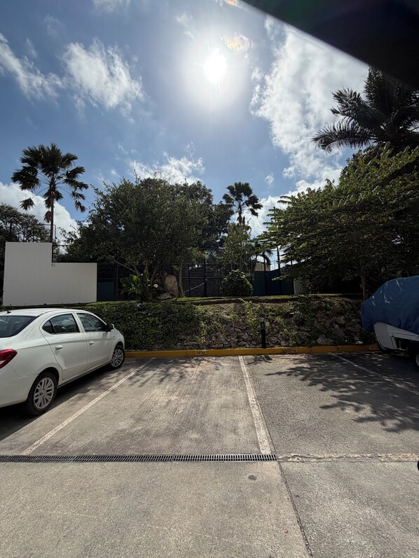 A parking area with a white car, a blue vehicle, and a building with a gated entrance. - Luxury apartment with a balcony in the Cumbres shopping plaza (Cancún)