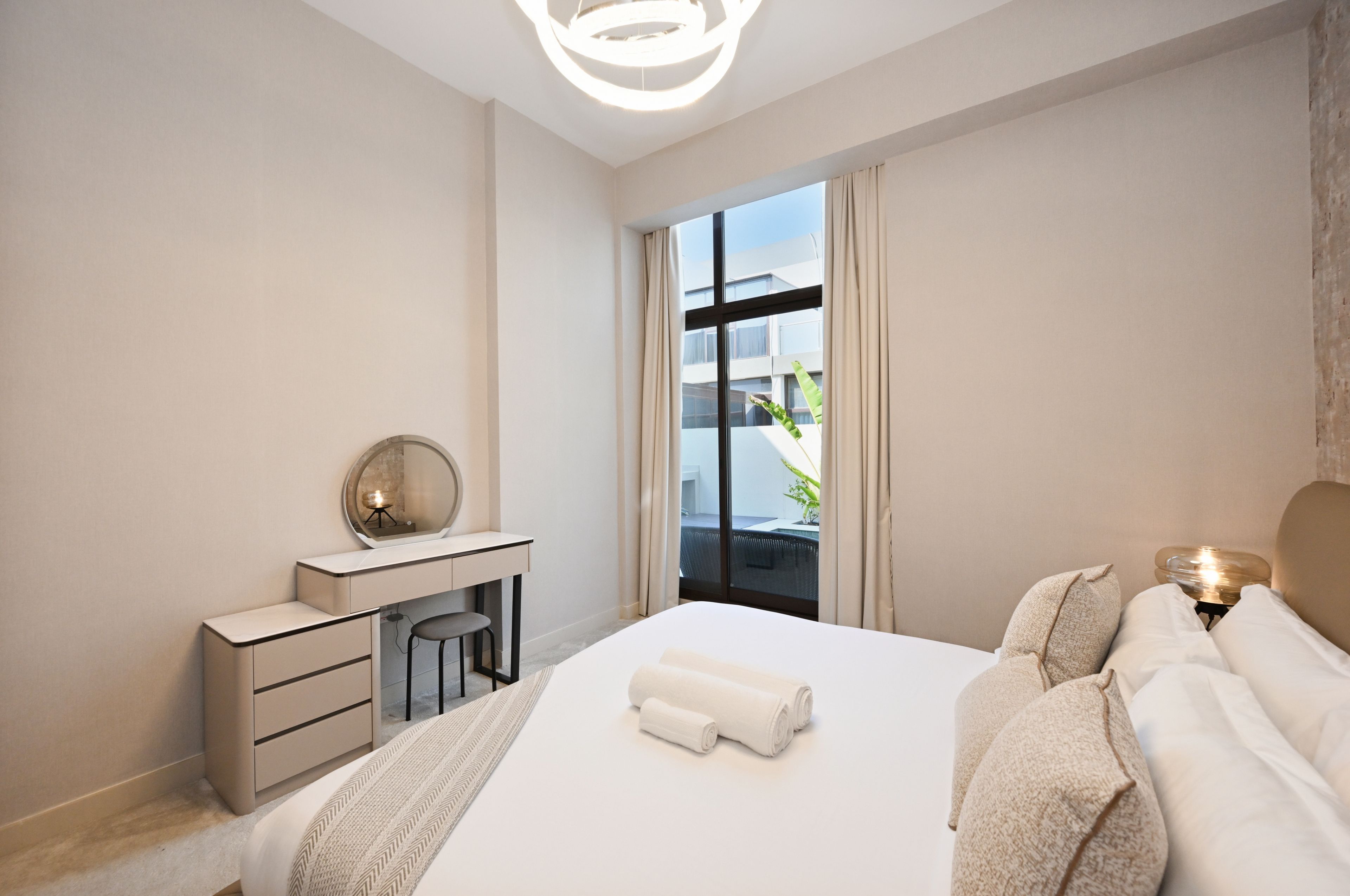A hotel room with a bed, a desk, a chair, a mirror, and a view of the outside.